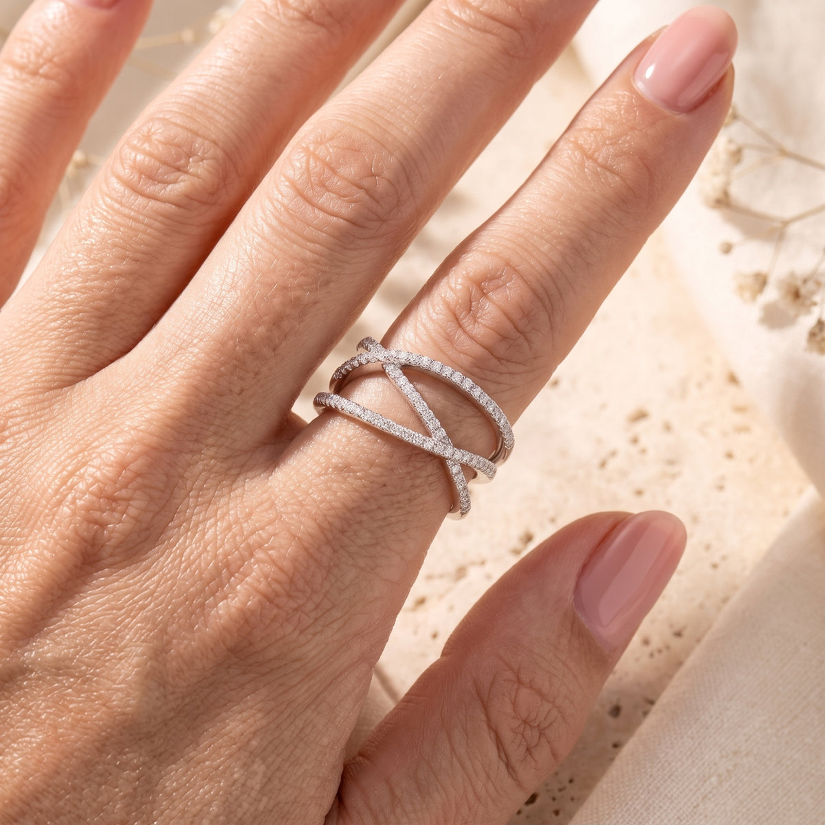 Overhead view of a hand wearing a silver crossover ring with multiple bands and clear pave stones.