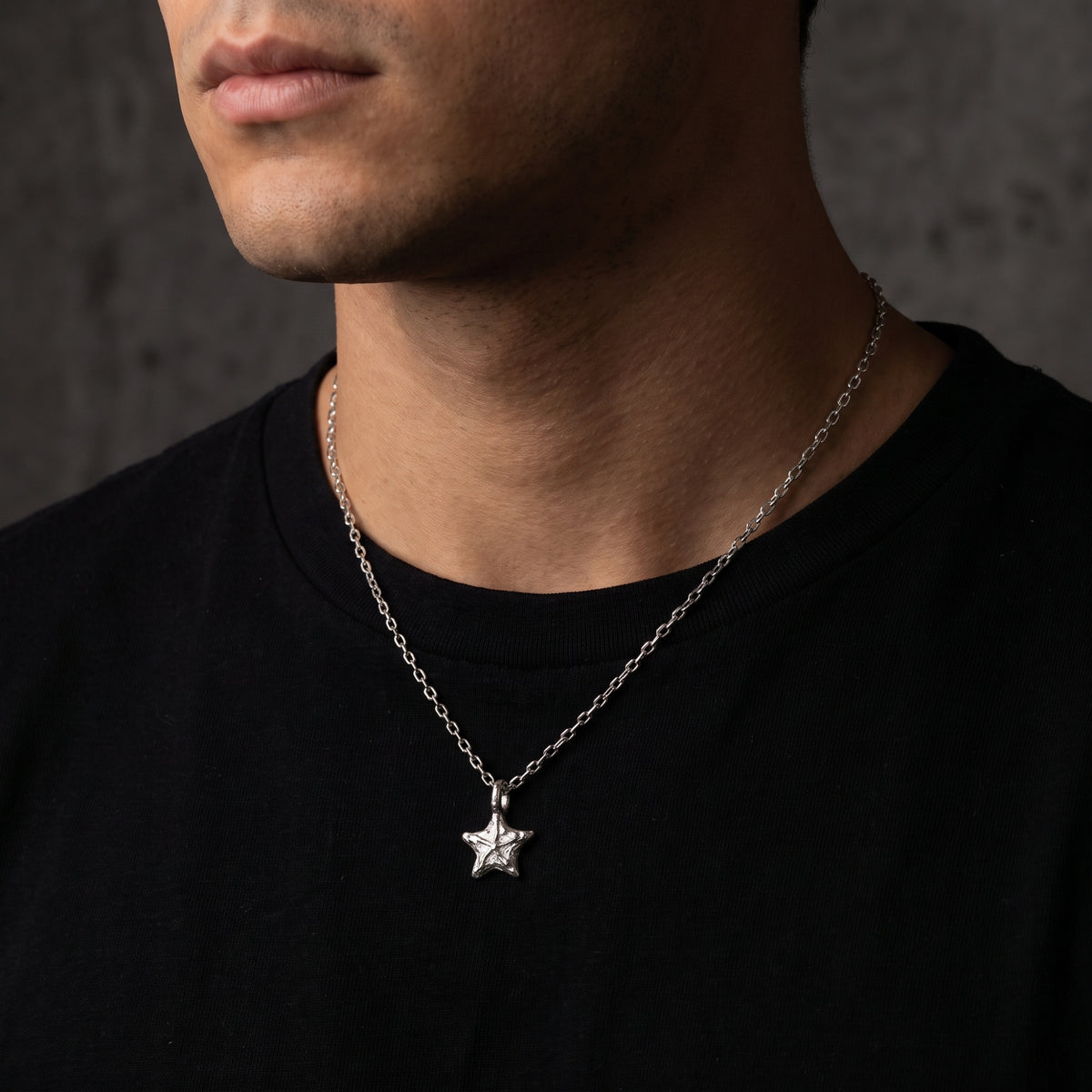 Man wearing the textured silver starburst necklace on a longer chain over a black shirt.