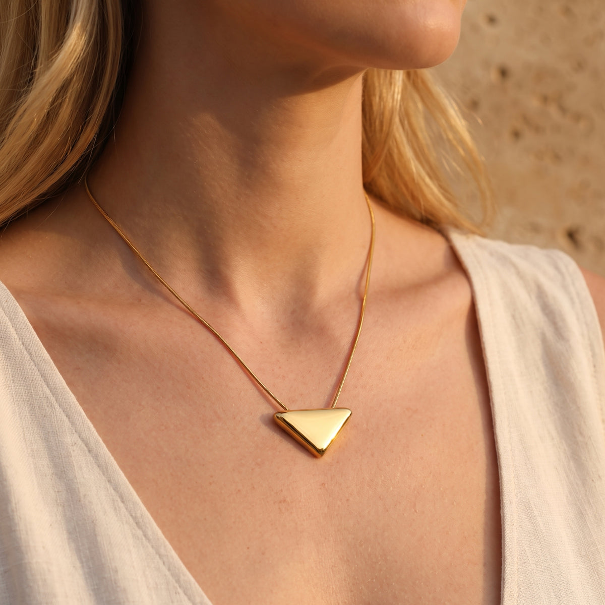 Angled profile view of a woman wearing the gold-tone triangle pendant necklace.