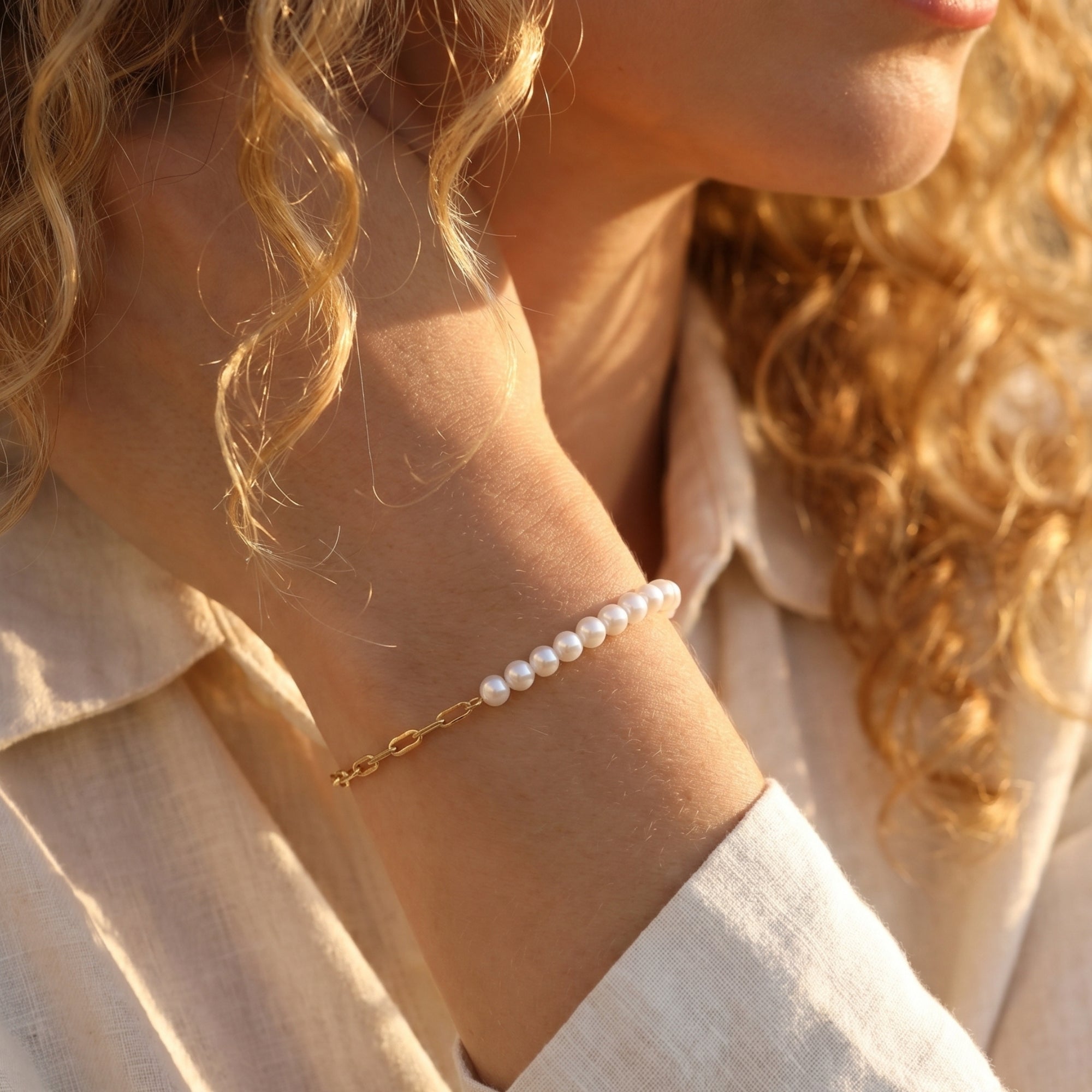 Side view of the gold chain and pearl bracelet worn on a model's wrist in warm sunlight.