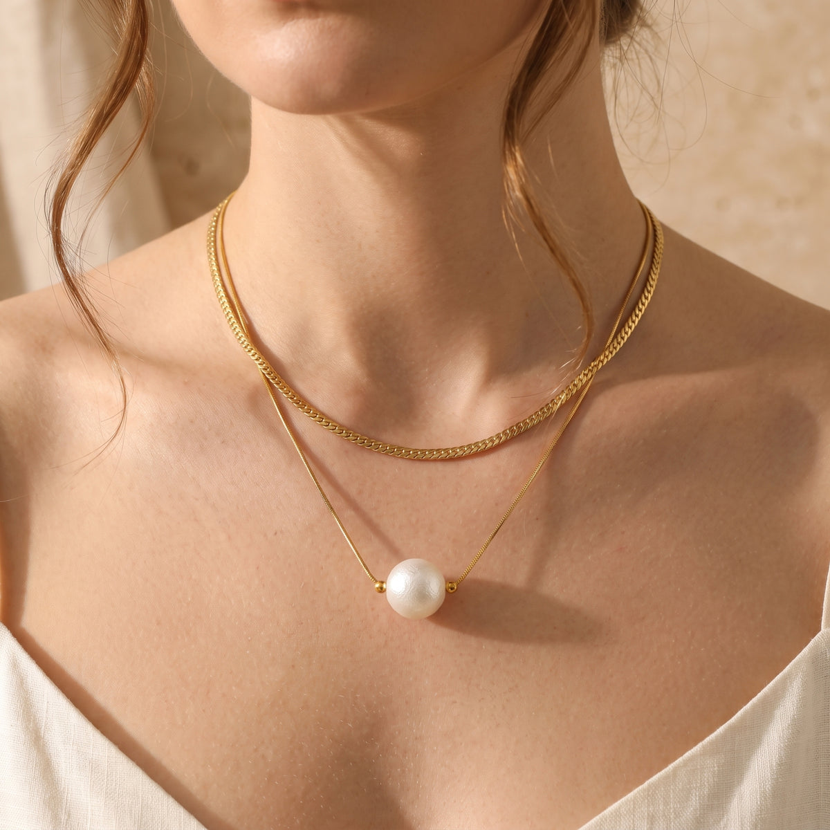 Close-up of a model wearing the gold-tone layered necklace with a white pearl pendant on her upper chest.