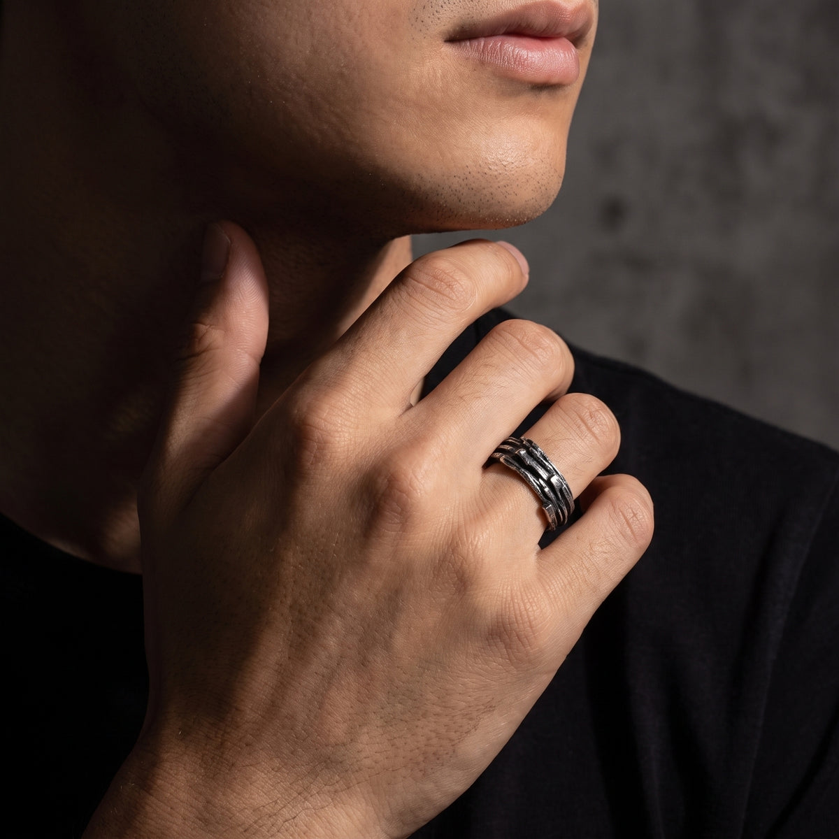 Close-up of a man wearing the textured oxidized silver open band ring near his neck against a black shirt.