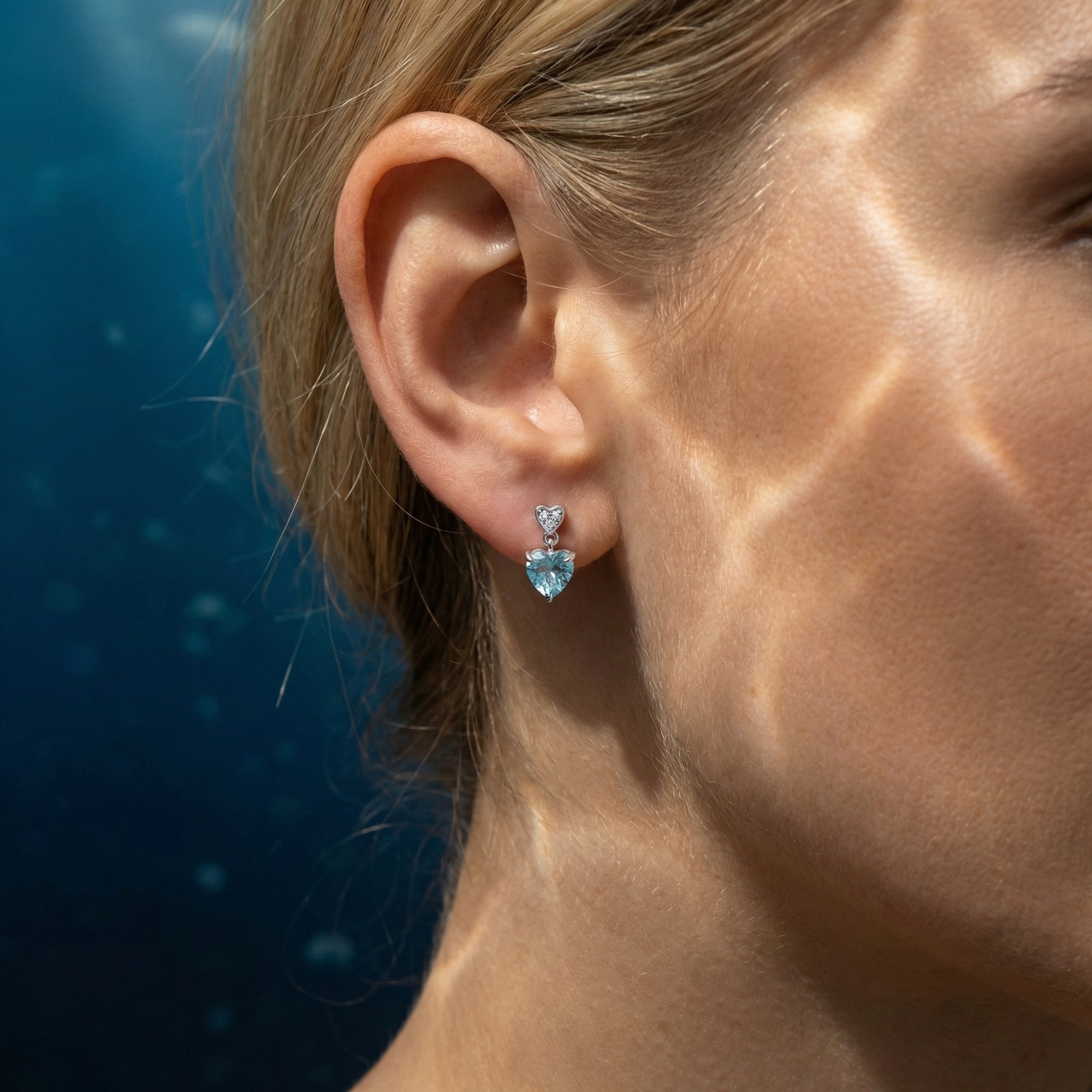Side profile of a model wearing an 18K white gold heart-cut aquamarine drop earring.