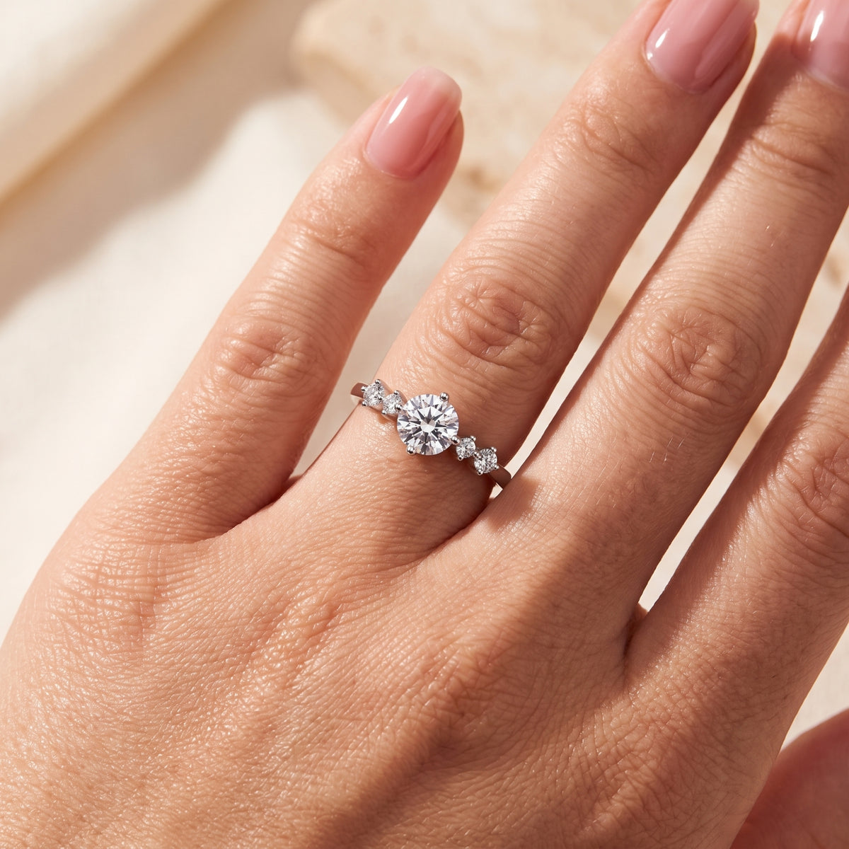 Close-up of the silver ring worn on a finger, showcasing its round center stone and flanking side accents.