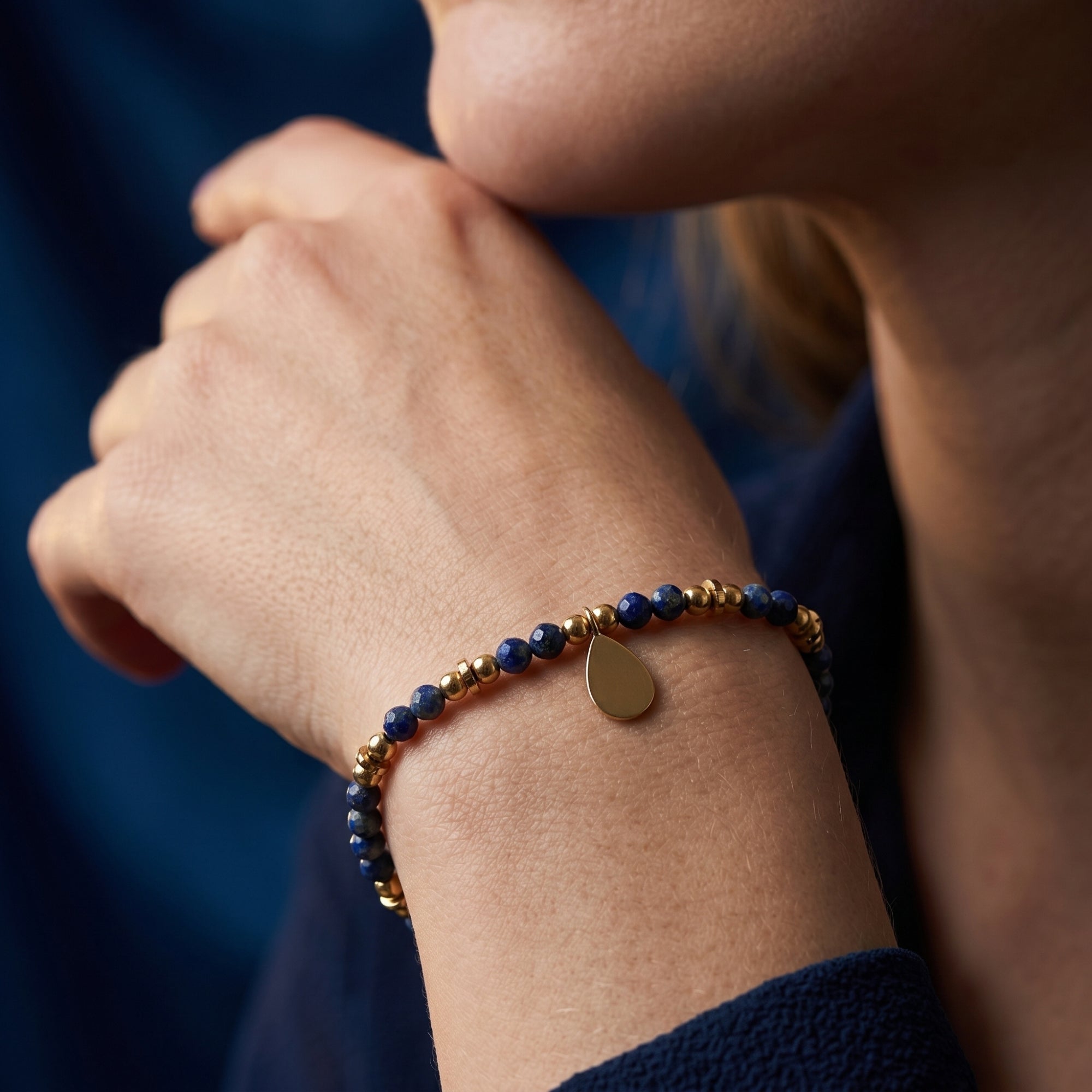 Woman wearing the gold plated faceted 3mm lapis bead bracelet with a dangling teardrop charm.