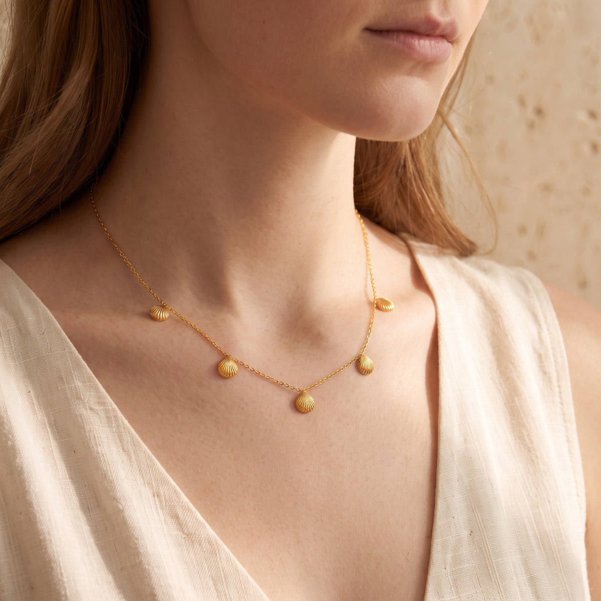 Close-up of a model wearing the gold-tone scallop shell station necklace with a cream sleeveless top.