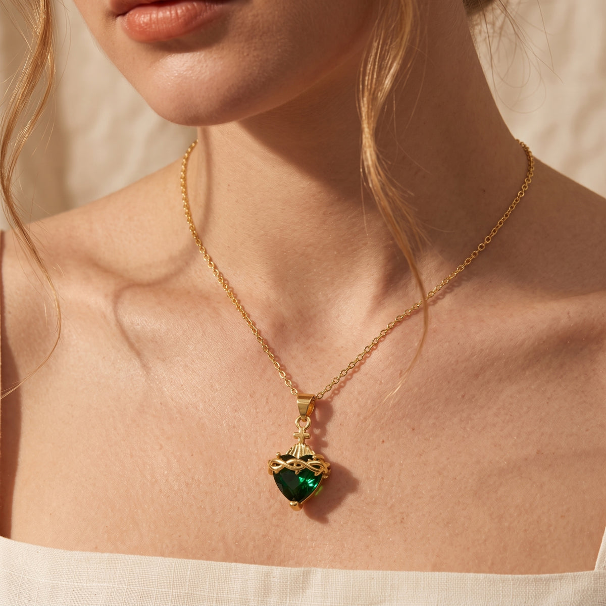 Close-up of a model wearing a gold-tone necklace with a heart-cut simulated emerald pendant and cross.