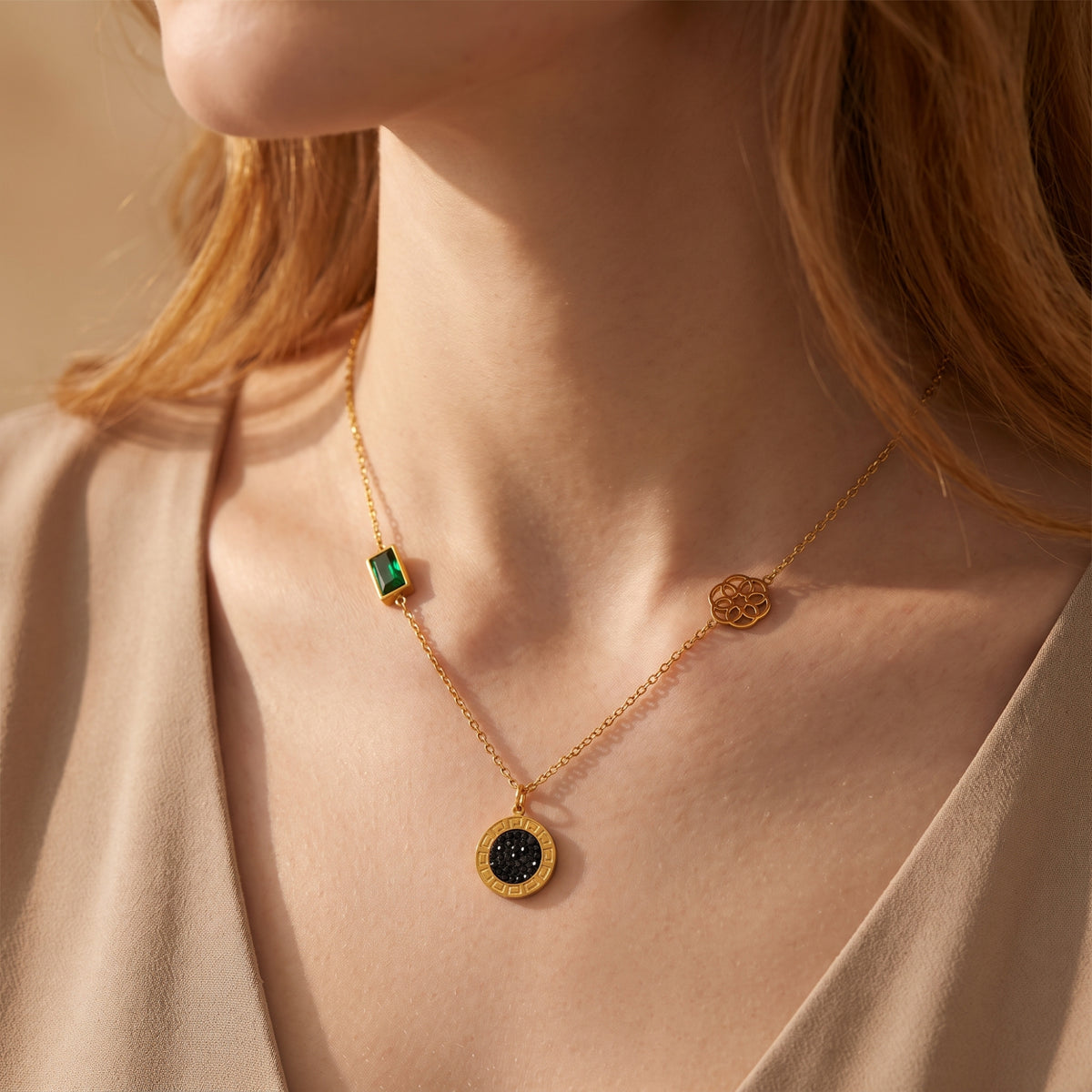 Close-up of a model wearing the gold-tone station necklace with green crystal and black medallion over a beige garment.