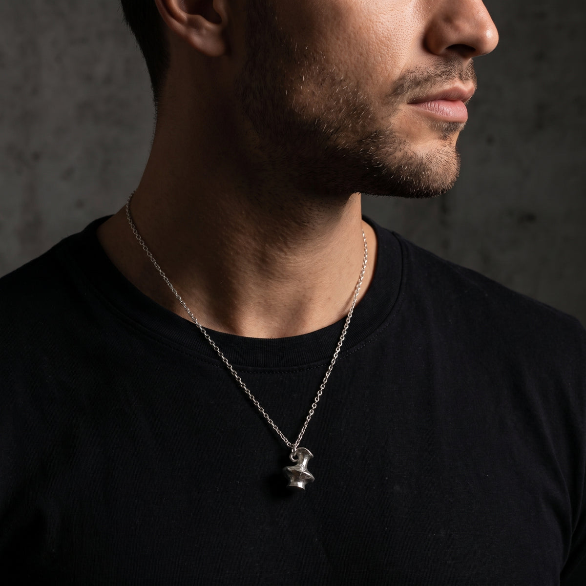 Side-angle view of a man wearing the silver vessel pendant necklace over a black T-shirt.