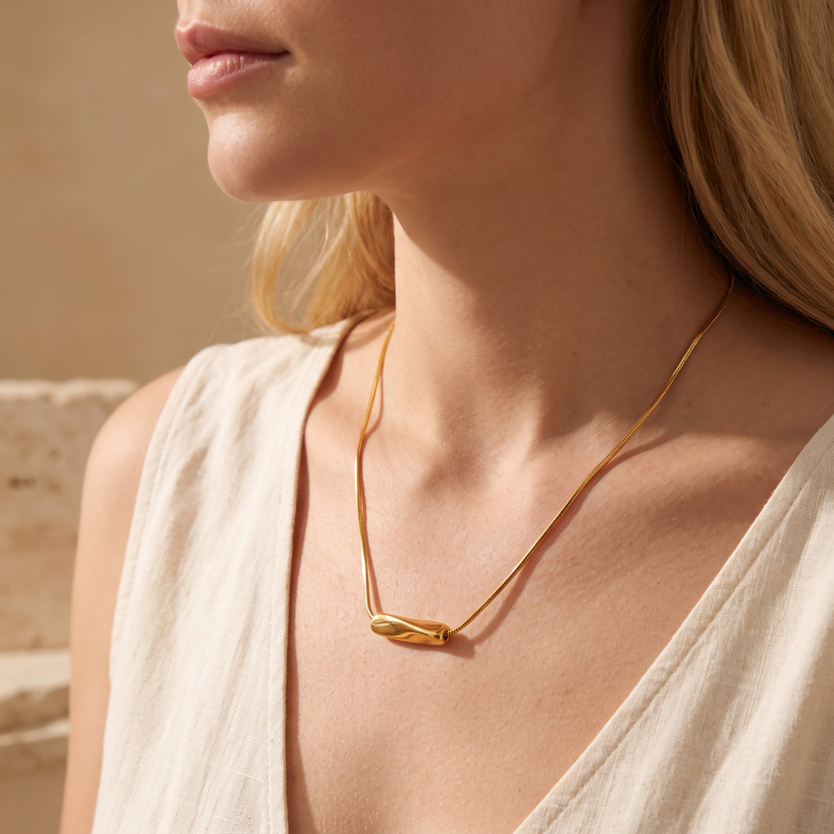 Model wearing the gold-tone wave slide necklace with a cream sleeveless V-neck top.