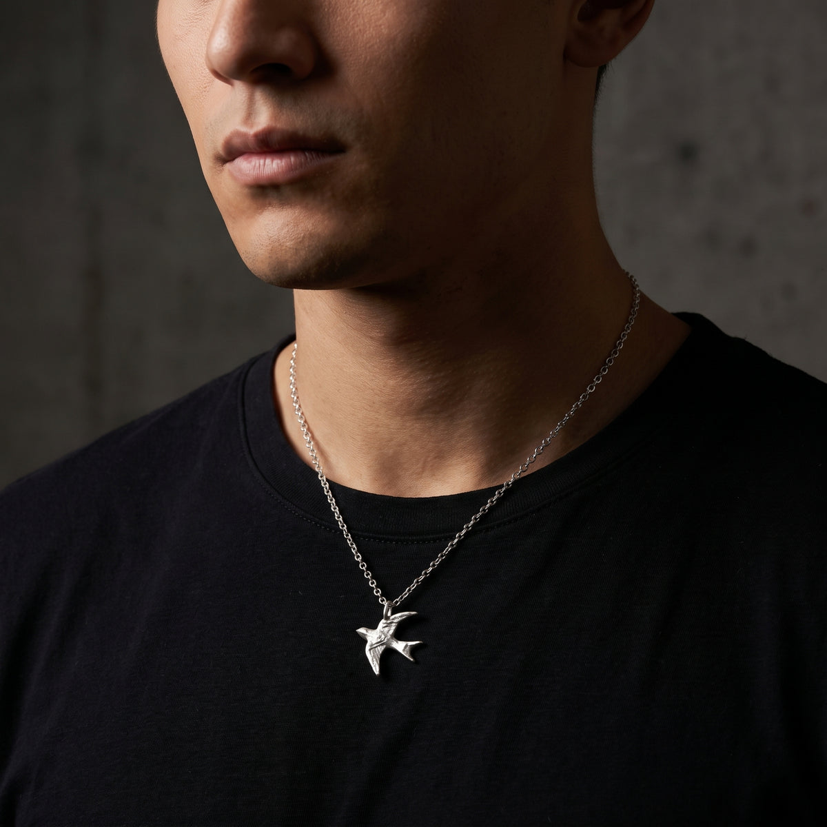Front-facing view of a man wearing the silver swallow pendant necklace over a black T-shirt.