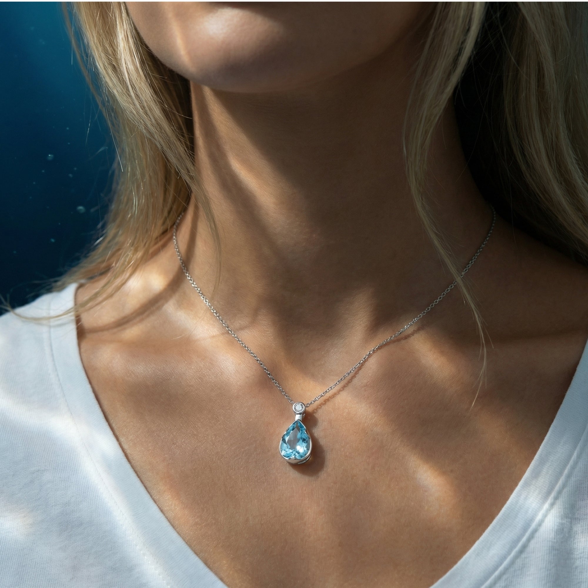 Pear cut aquamarine pendant necklace in platinum, worn by a model in a white shirt with soft sunlight.