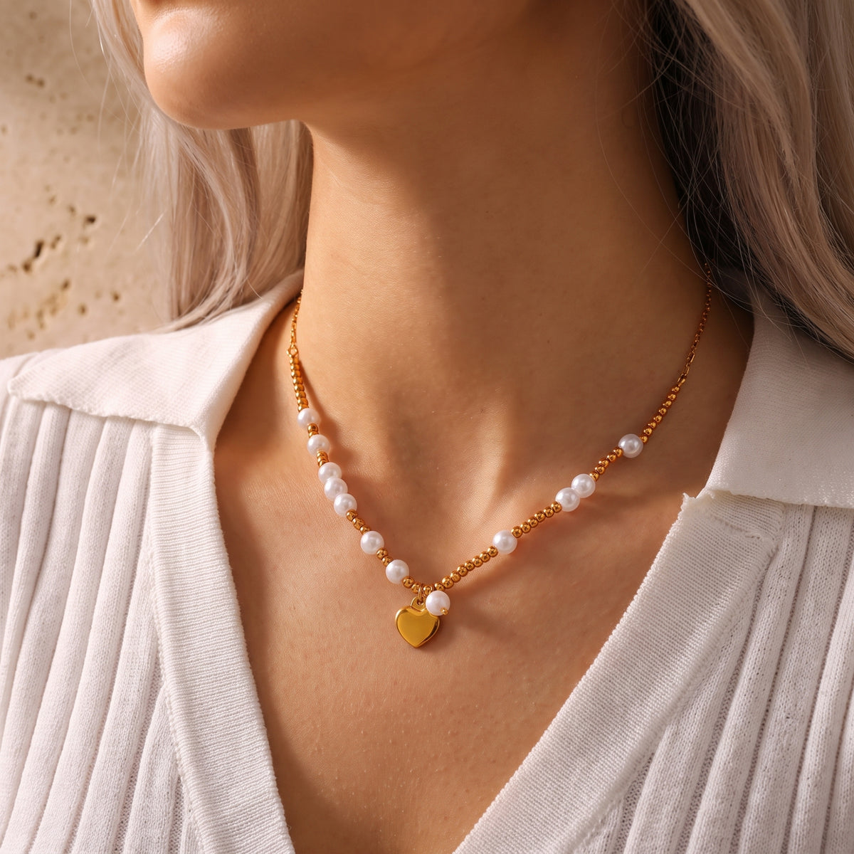 Angled view of a model wearing a white pearl and gold-tone heart pendant necklace with a white ribbed sweater.