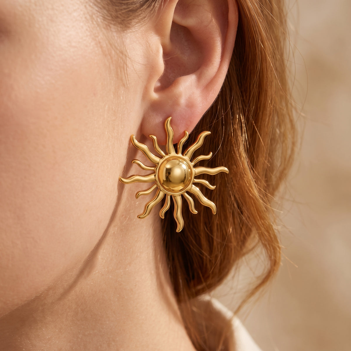 Close-up view of the gold-tone sunburst stud earring worn on an earlobe, framed by brown hair.