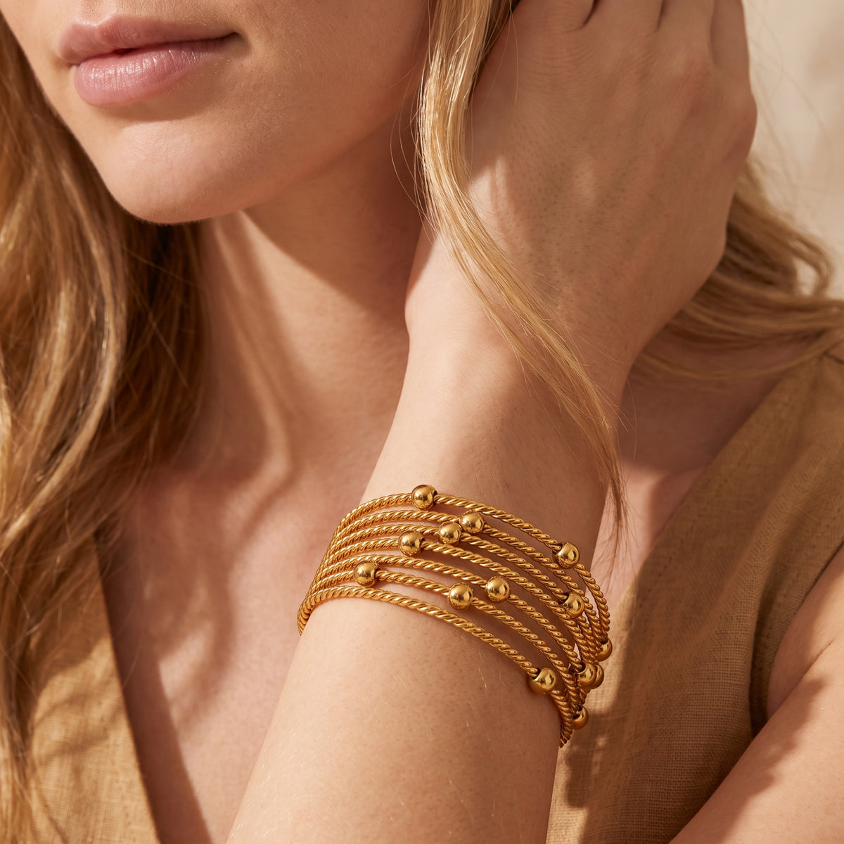 Close-up of a model in a beige top wearing the gold-tone multi-strand cable cuff near her face.