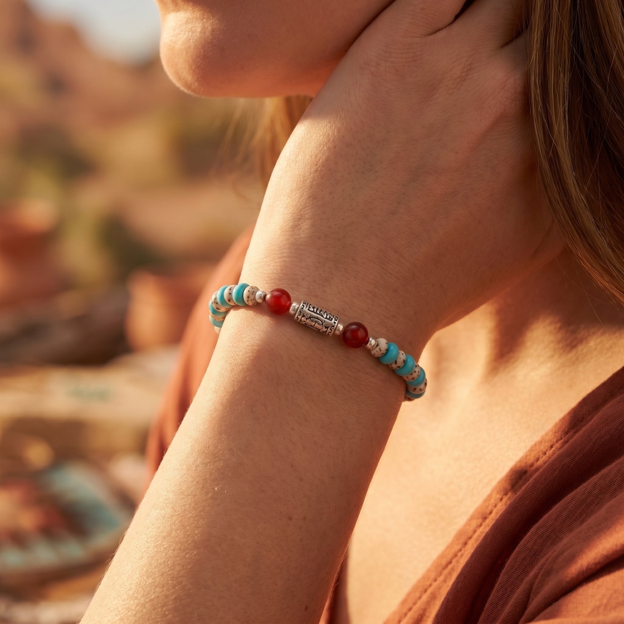 Close-up of the turquoise and carnelian beaded bracelet with a silver mantra bead worn on a model's wrist.