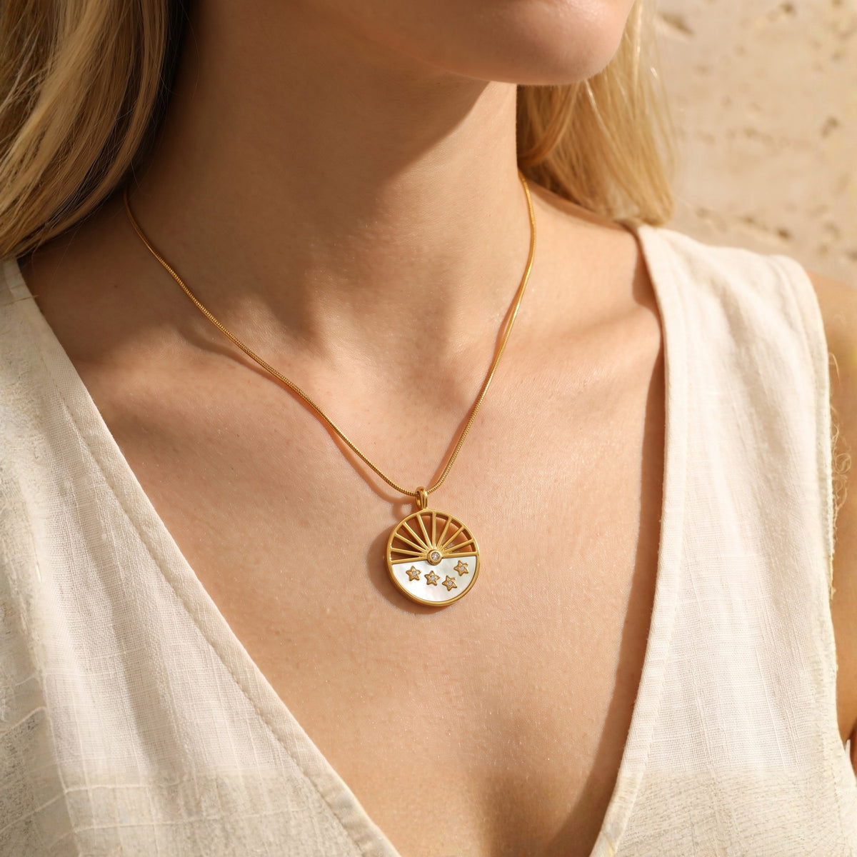 Model wearing the gold-tone celestial sunburst necklace over a white sleeveless v-neck top.