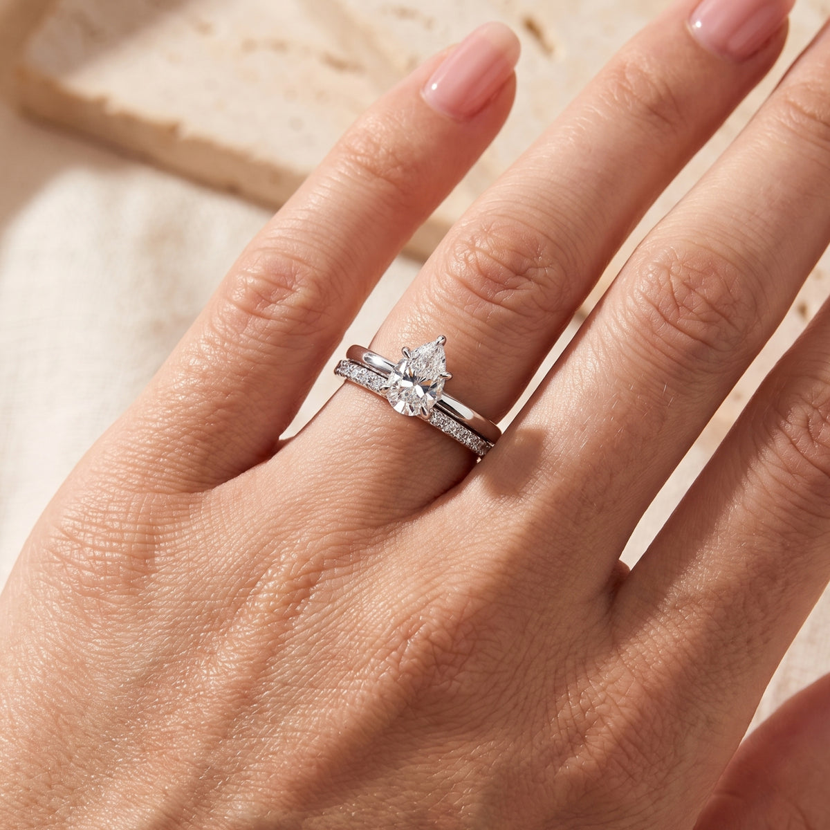 Close-up of a hand wearing the two-ring set with a pear-cut solitaire and pavé band.
