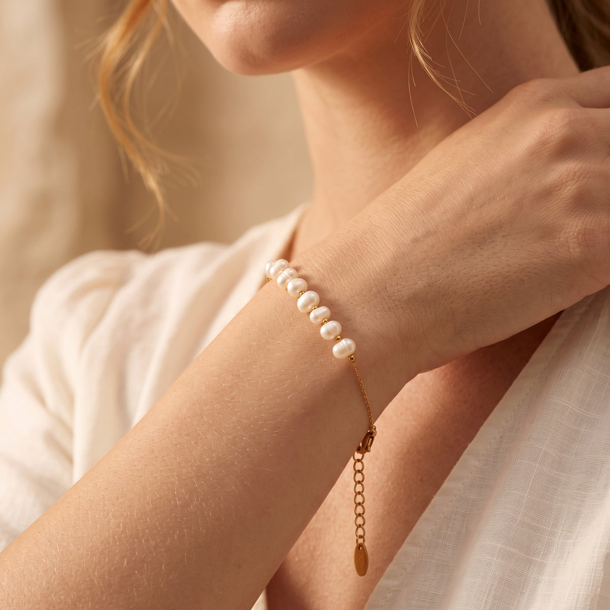 Gold-tone pearl station bracelet worn on a wrist as the model's hand rests near her neck, extender chain visible.