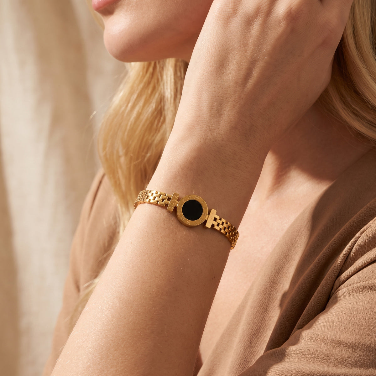 Gold-tone Roman numeral link bracelet worn on a wrist against a neutral beige outfit.