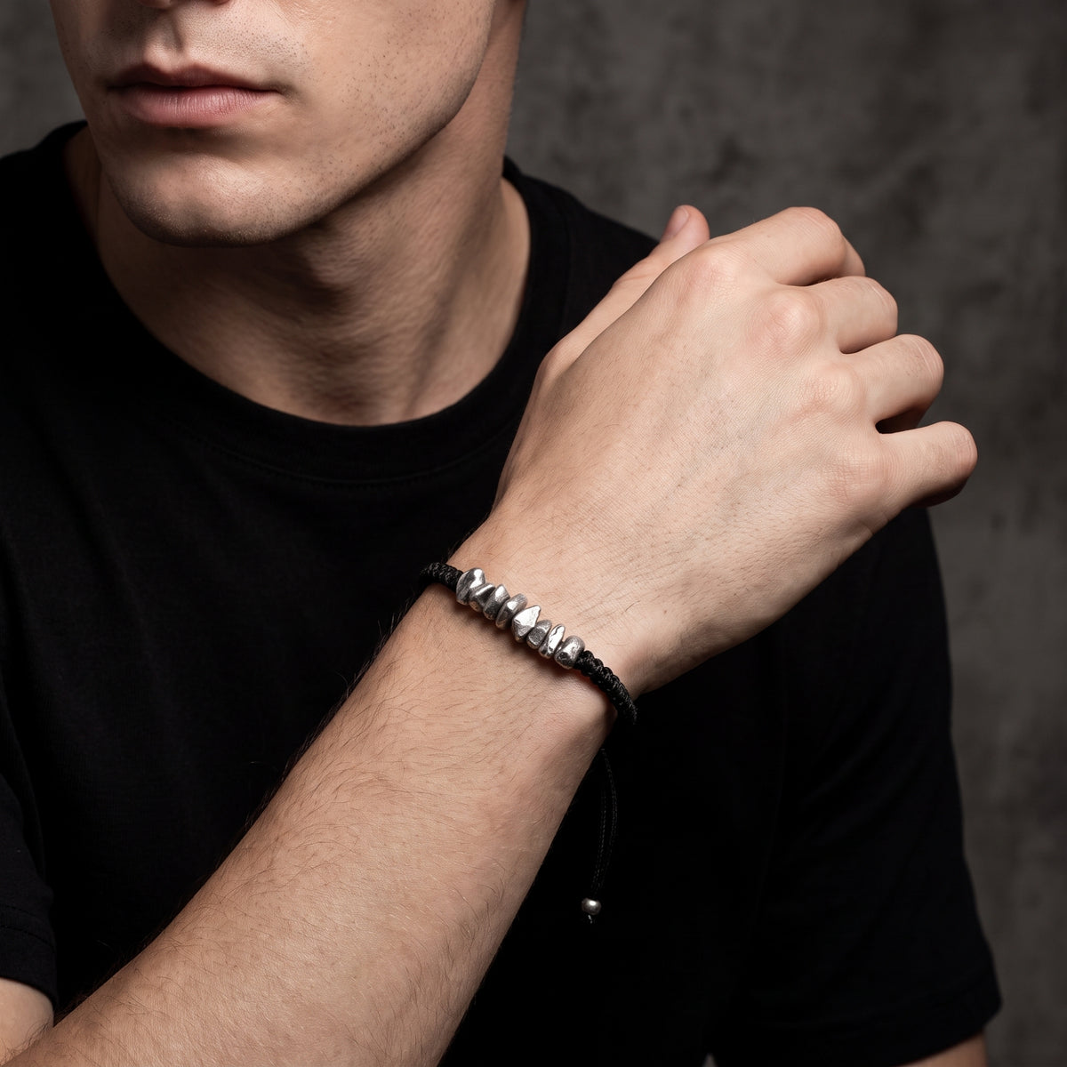 Man wearing the black cord bracelet with silver nuggets on his wrist in a three-quarter view.