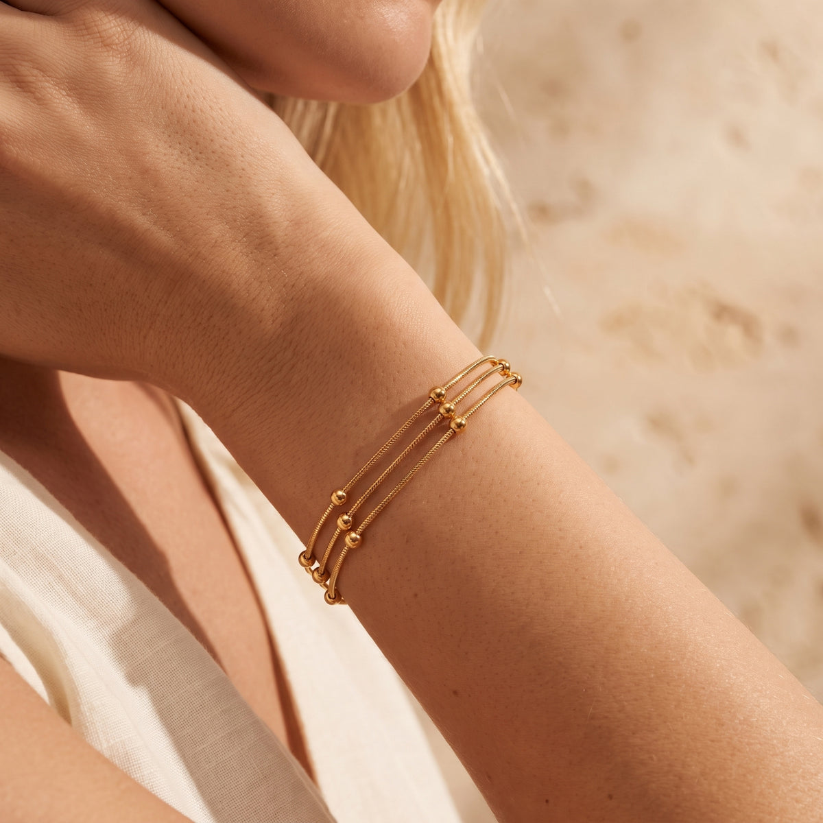 Close-up angled view of a model wearing the gold three-strand bead bracelet on her forearm.