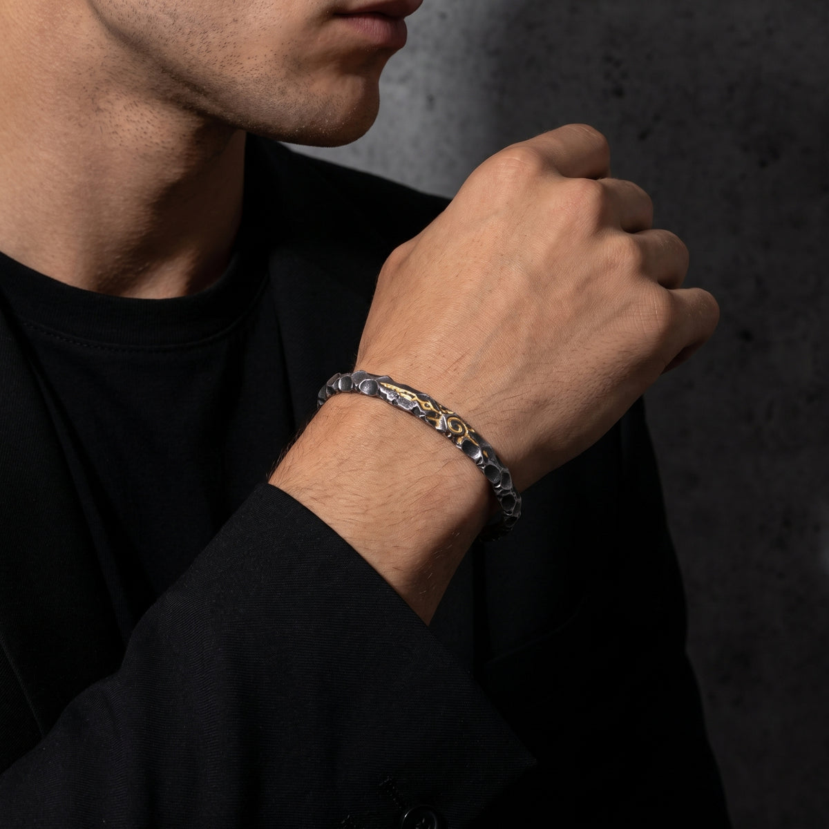 Man wearing the hammered silver sigil cuff bracelet on his wrist with his hand raised across his chest.