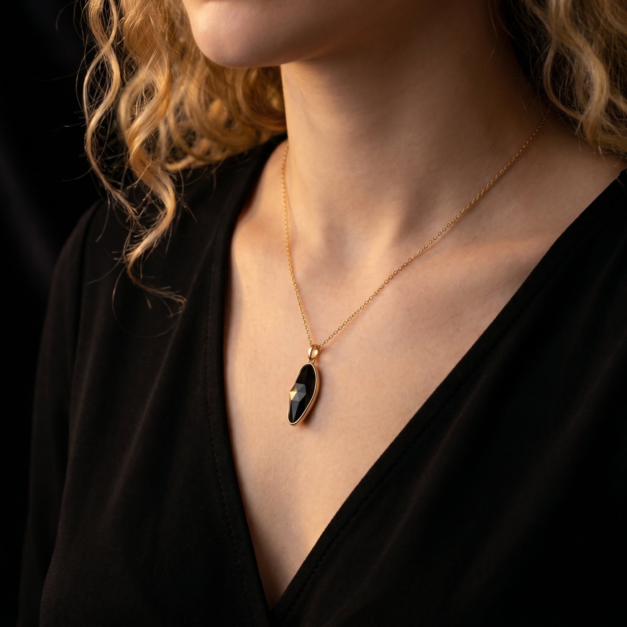 Side view of the gold Morgana necklace with a black onyx pendant worn by a model in a black V-neck top.