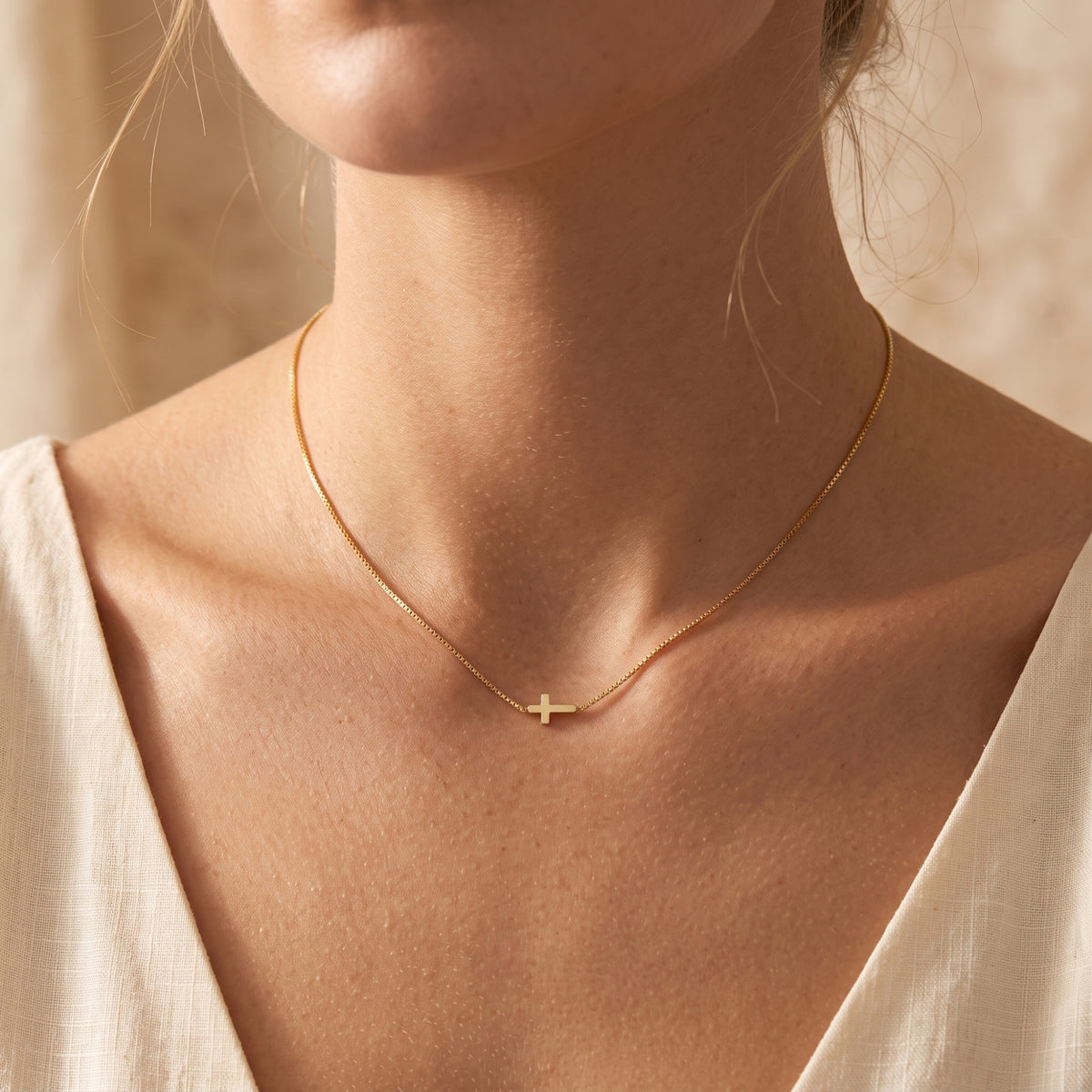 Front-facing model wearing the gold-tone sideways cross necklace with a white V-neck top.