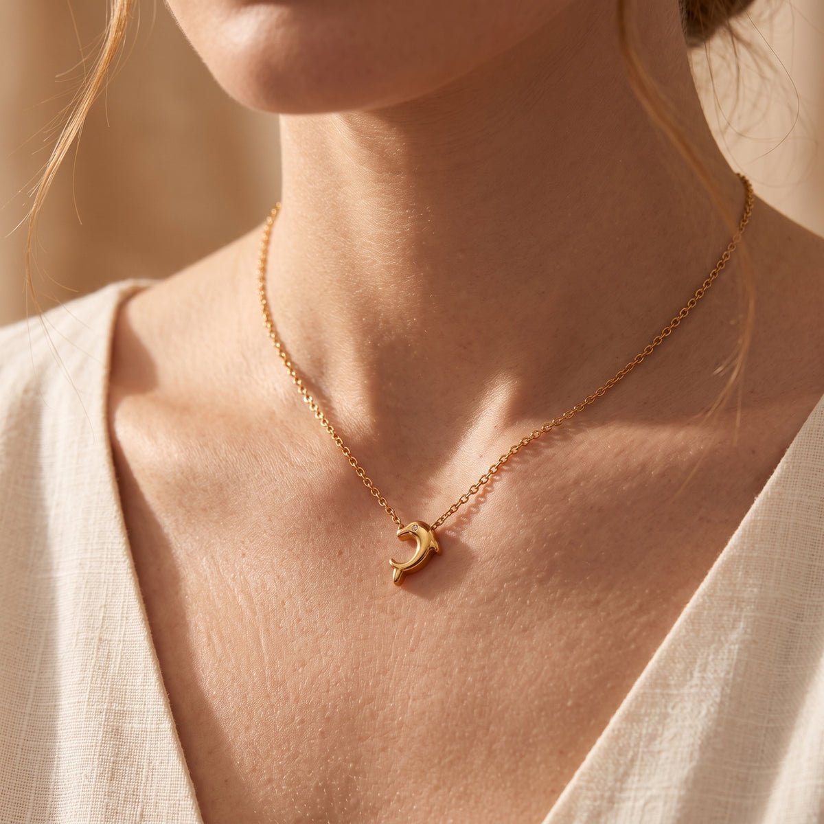 Model wearing the gold-tone dolphin pendant necklace paired with a cream linen top.