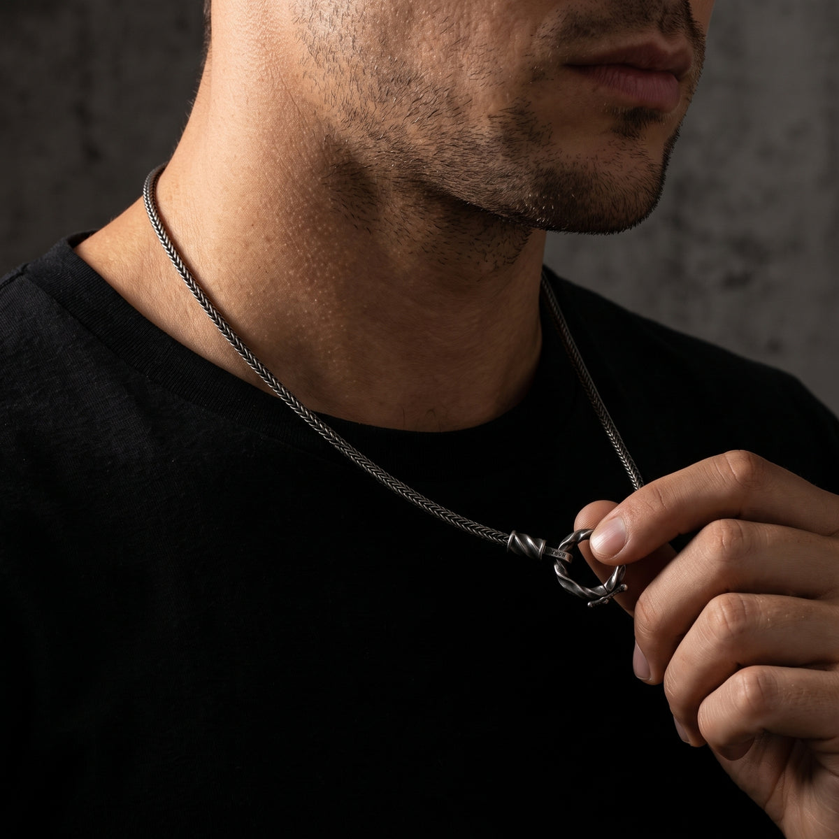 Close-up of a man holding the silver twisted ring pendant while wearing the necklace.
