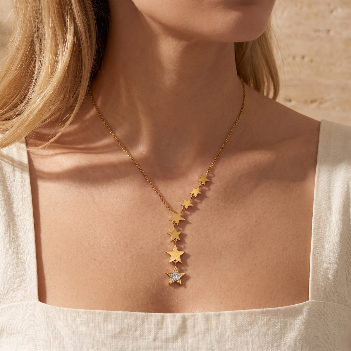 Front view of a model wearing the gold-tone star lariat necklace with a white square-neck top.
