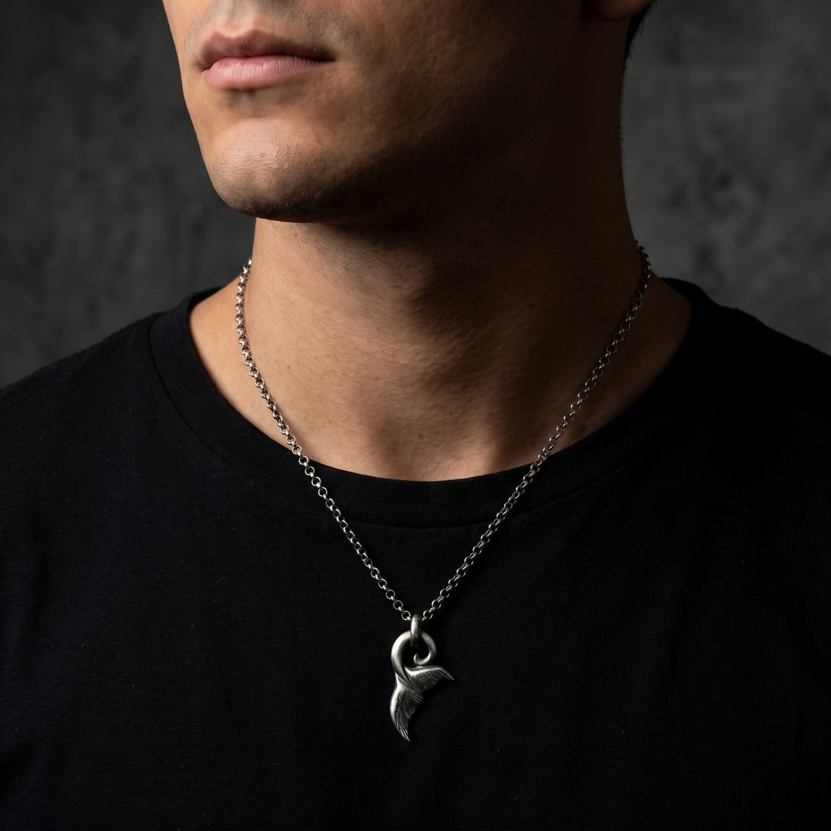 Front-angle view of a man wearing the silver whale tail fluke pendant over a black shirt.