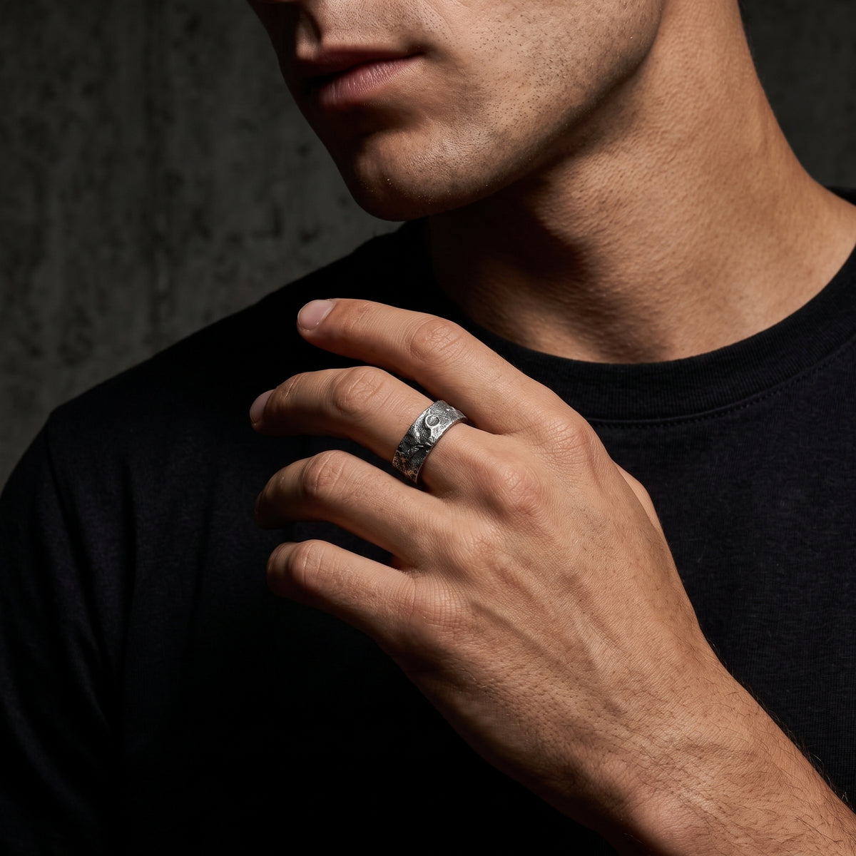 Textured silver open-band ring worn on a model’s middle finger against a black shirt and gray backdrop.