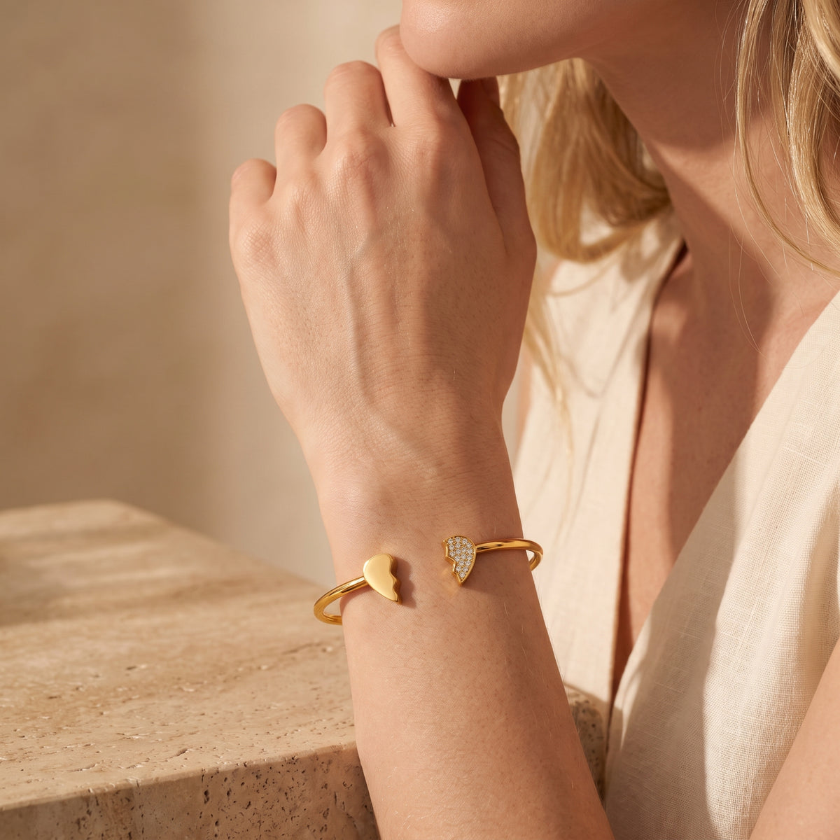 Person wearing the gold-tone broken-heart open cuff bracelet while resting a hand near the chin.