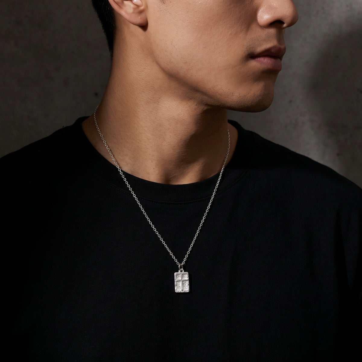 Angled view of a man wearing the silver textured cross pendant necklace over a black t-shirt.