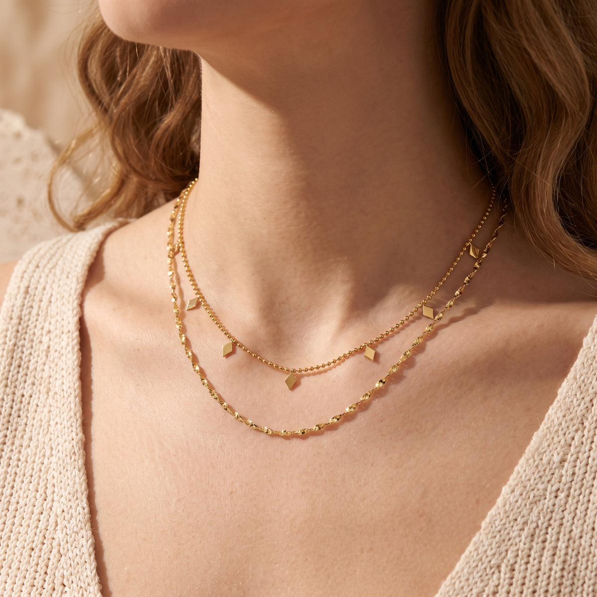 Front view of a model wearing a layered gold-tone necklace with diamond-shaped drop charms.