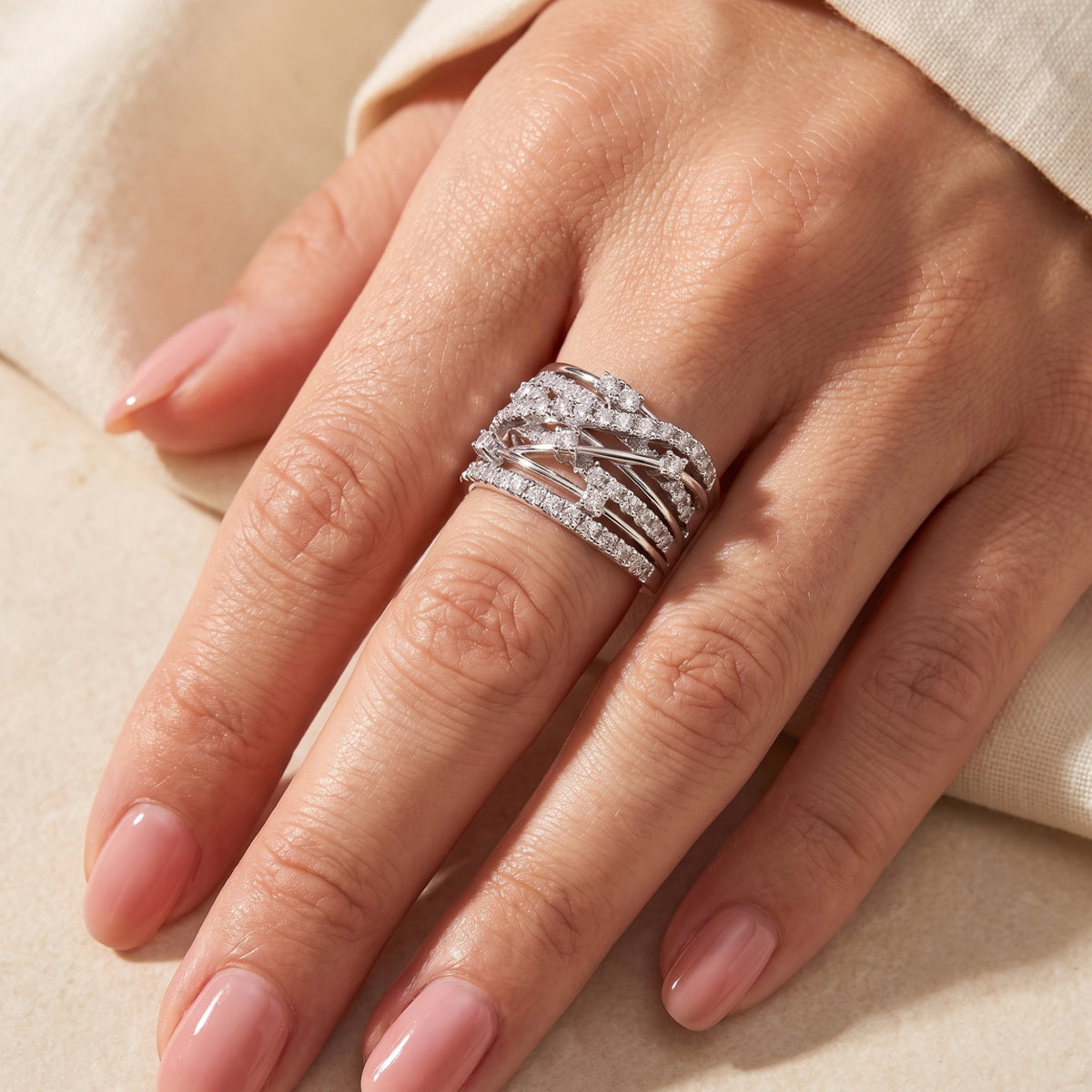 Close-up of a hand with polished nails wearing a wide silver criss-cross ring with clear accents.
