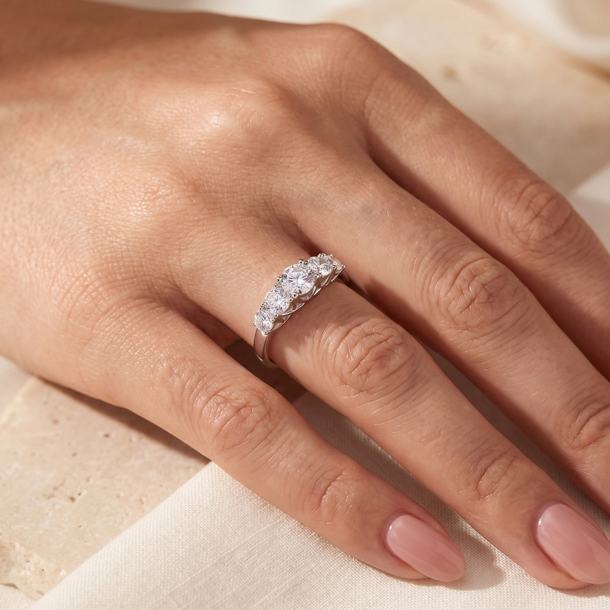 Close-up of a hand resting on fabric while wearing the silver ring with five graduated round stones.