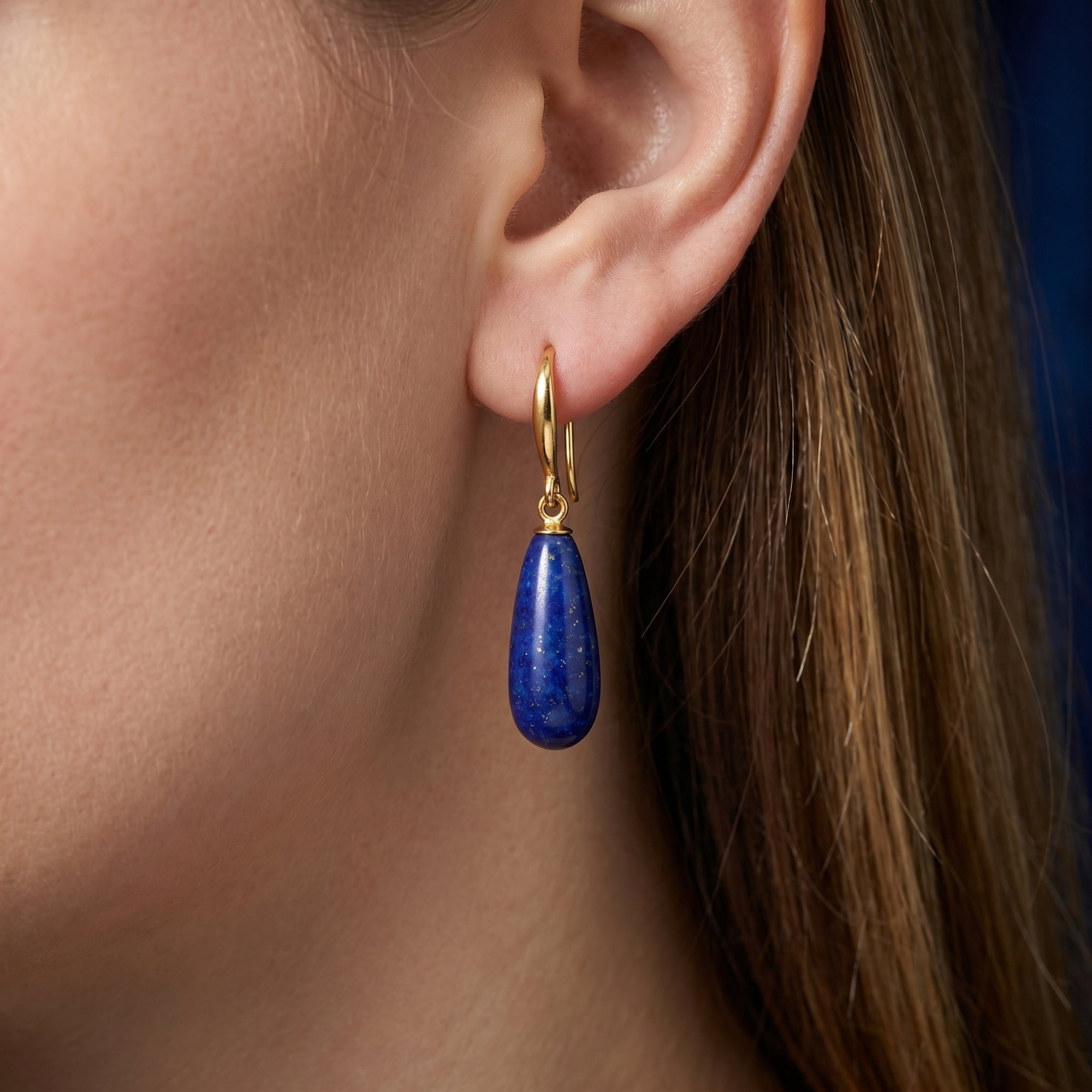 Side view of a pear-shaped natural lapis lazuli drop earring in 18K gold plating worn on a model's ear.