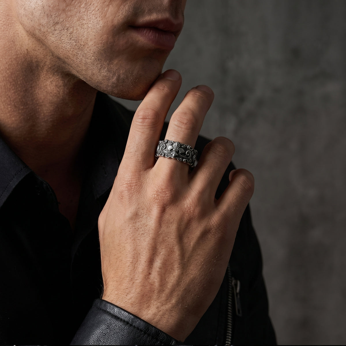Side view of a model wearing the silver fleur-de-lis ring on his middle finger with his hand near his chin.