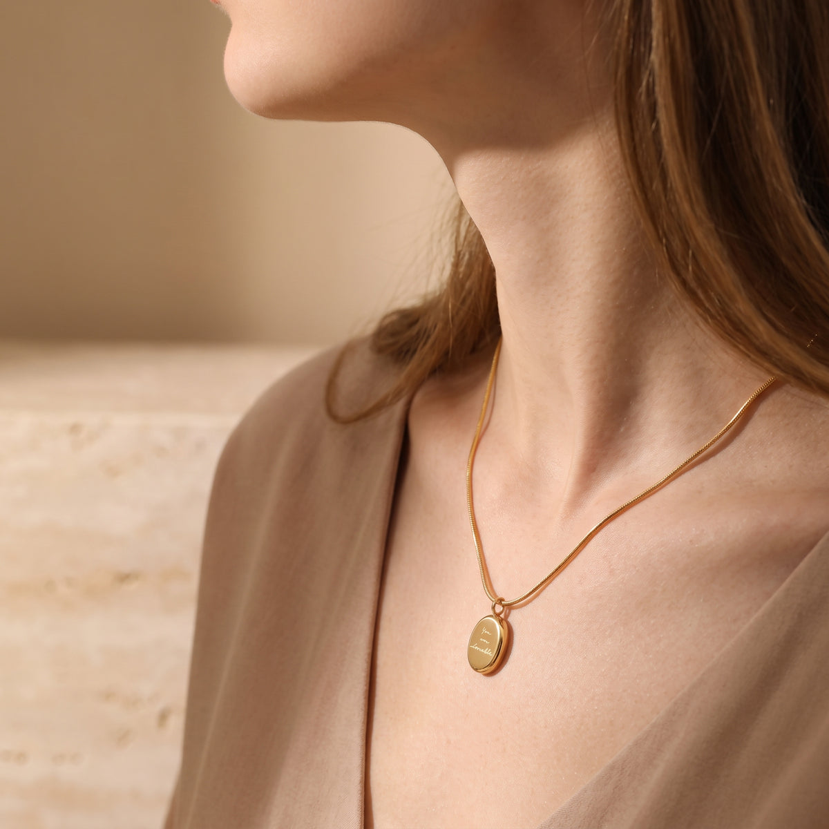 Side-profile view of a woman wearing the gold-tone oval medallion necklace over a beige V-neck outfit.
