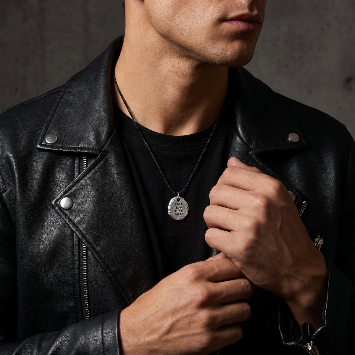 Man wearing the engraved silver pebble necklace over a black shirt and beneath a black leather jacket.