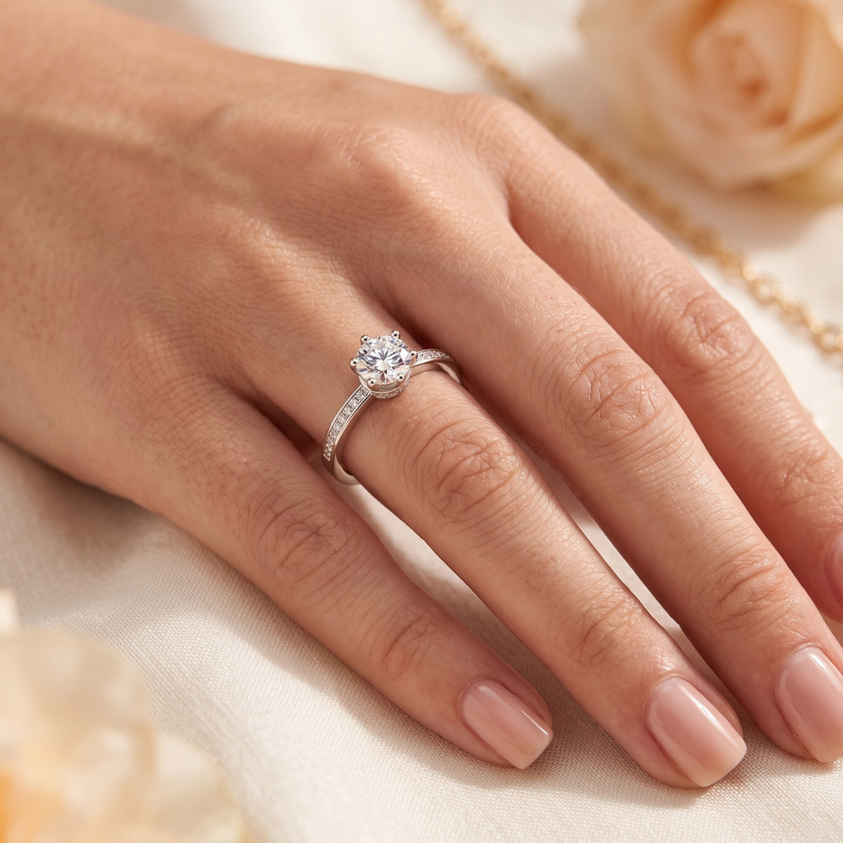 A hand wearing the silver solitaire ring against light fabric, showcasing the round clear stone and pavé accents.