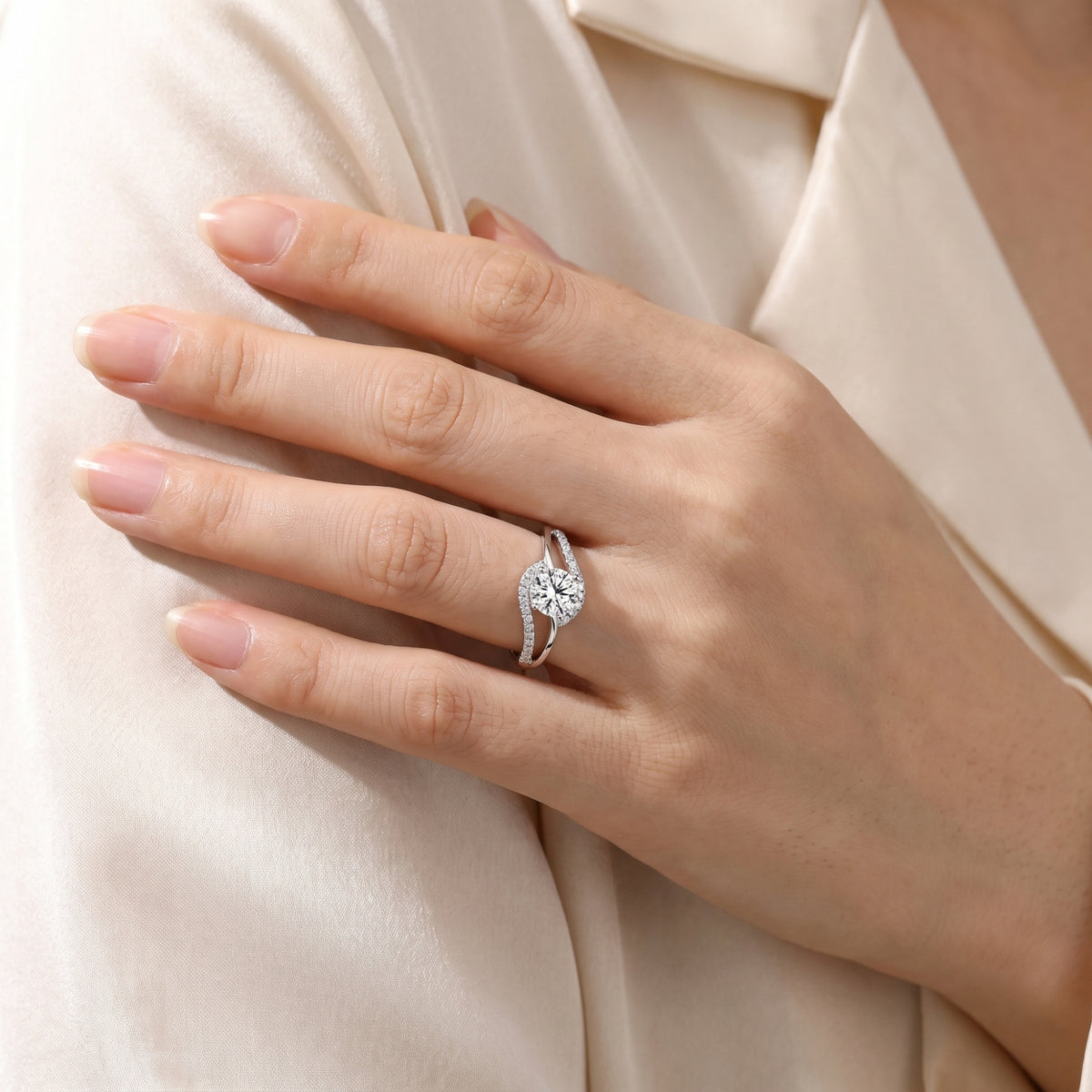 Hand wearing the silver bypass ring with a round clear center stone and pavé accents against white fabric.