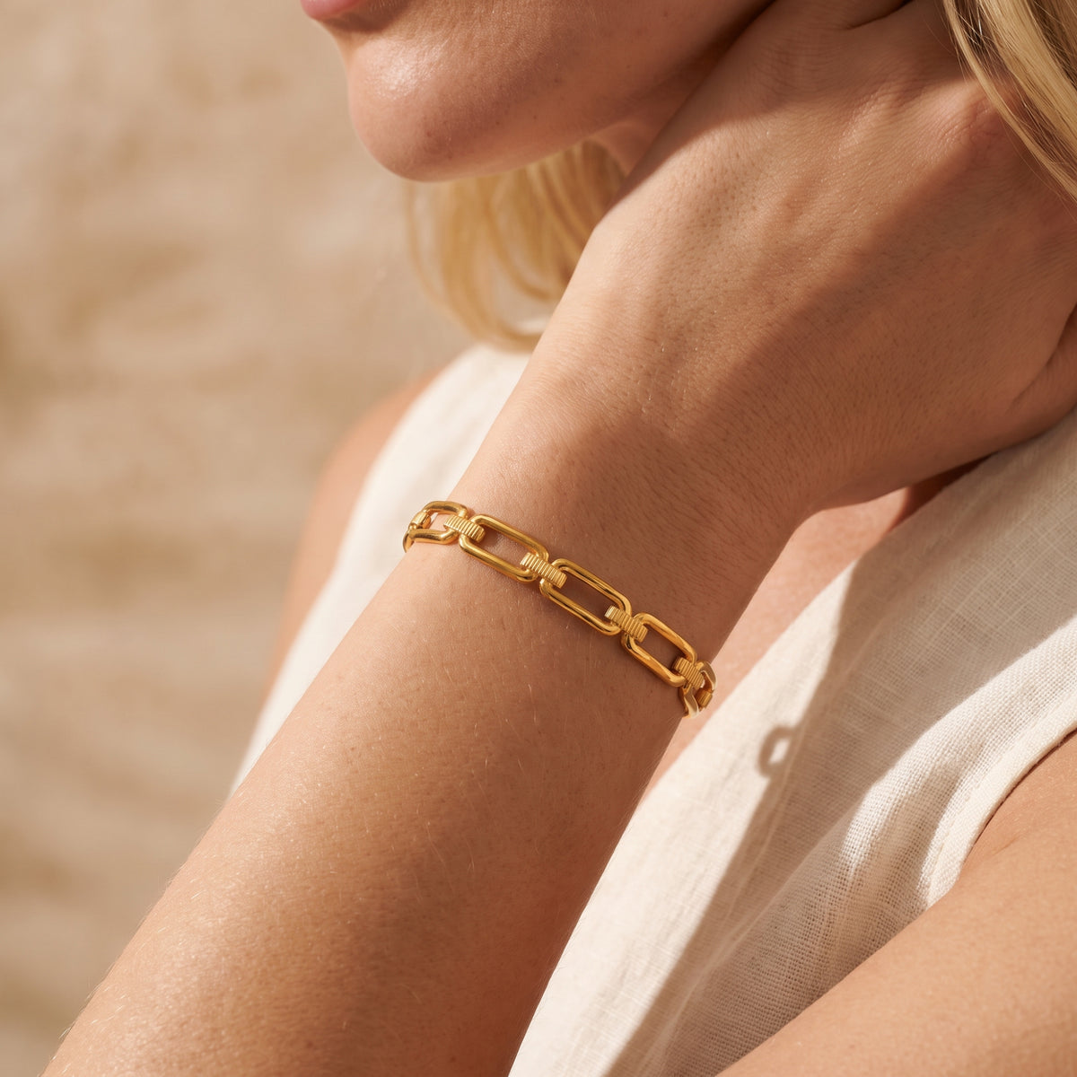 Gold-tone paperclip link bracelet worn on a model’s wrist beside a white garment.