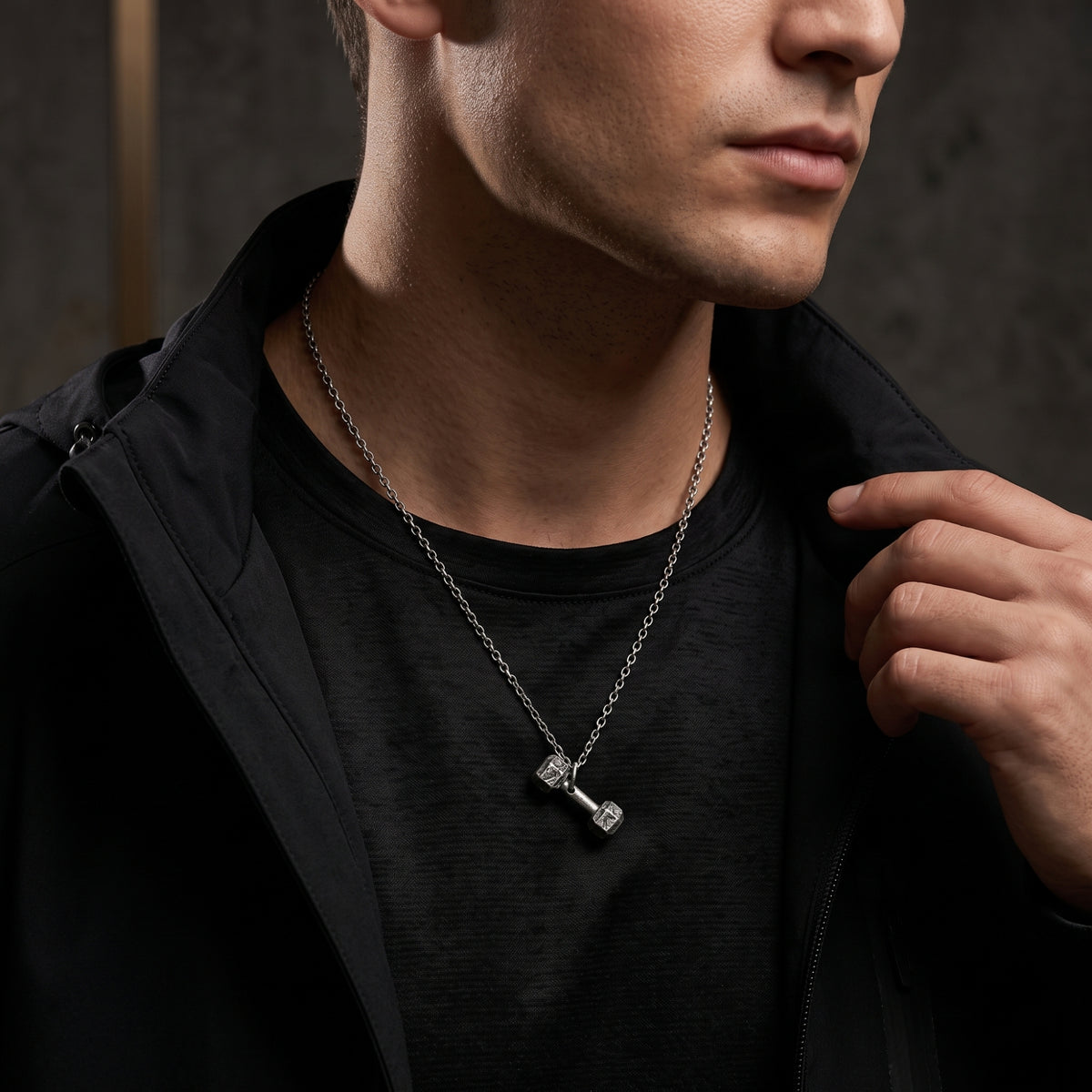 Model wearing a fine silver dumbbell pendant necklace over a black shirt and open jacket.