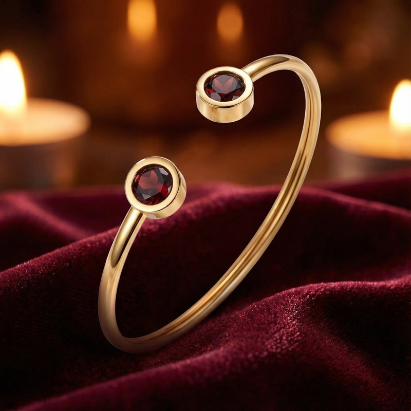 Gold ion-plated steel cuff bracelet featuring two round simulated garnets on a red velvet background.