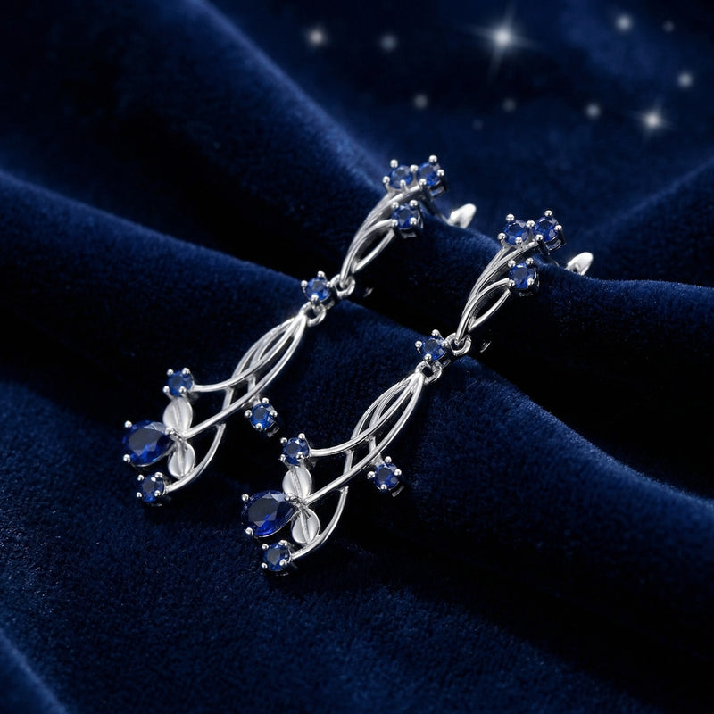 Side view of sterling silver vine drop earrings featuring deep blue simulated sapphires on a velvet background.