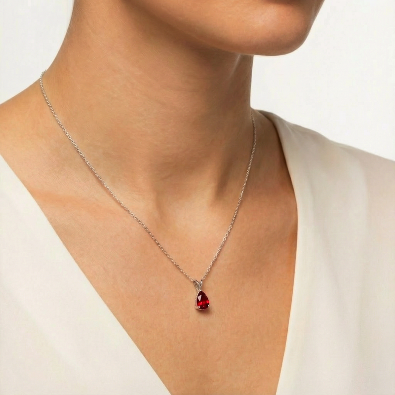 Sterling silver necklace with a pear cut red birthstone pendant worn by a model.